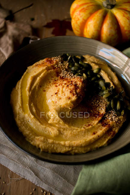 Set of yummy pumpkin hummus with seeds on cloth napkin placed on lumber tabletop with dried autumn leaves — Stock Photo