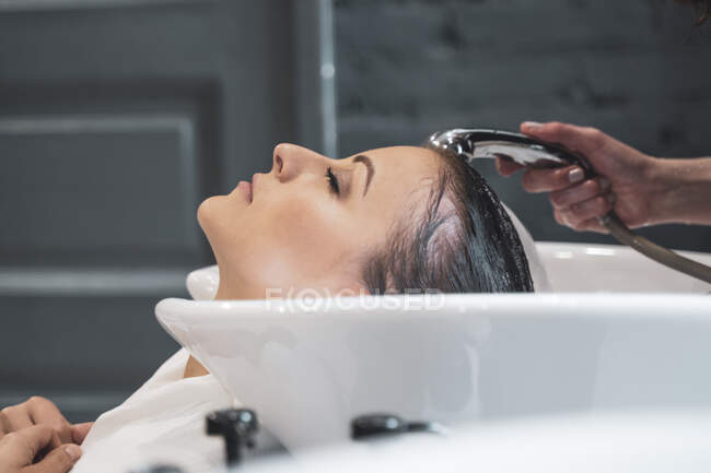 Styliste lavage des cheveux à jeune femme — Photo de stock