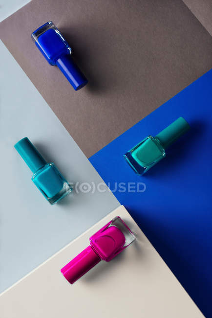 Esmaltes de uñas multicolores sobre fondo de patrón geométrico de colores - foto de stock