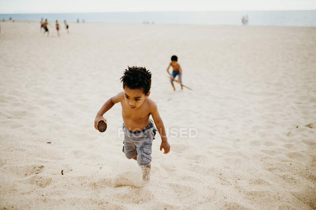 African American boy playing on sandy shore near sea — Stock Photo