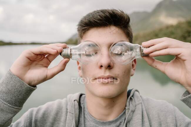 Young teenager boy with a couple of light bulbs in front of his closed eyes innovation and imagination concept — Stock Photo