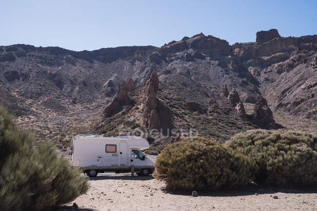 Caravane itinérante sur le bord de la route dans le désert sauvage à côté des buissons sur fond de montagne pierreuse au soleil — Photo de stock
