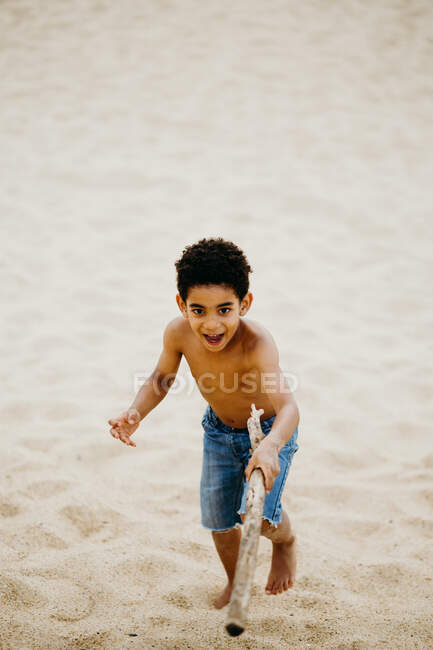 Engraçado menino afro-americano com vara jogando na costa arenosa perto do mar — Fotografia de Stock