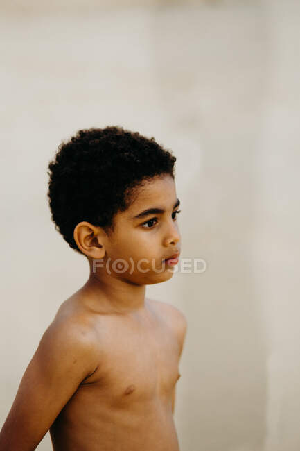 Seitenansicht des entzückenden, hemdlosen afroamerikanischen Jungen, der wegschaut, während er auf verschwommenem Strand-Hintergrund steht — Stockfoto