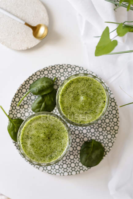 Здоровый зеленый смузи из шпината, авокадо и киви, яблоко и лимон в стаканах на узорной тарелке — стоковое фото