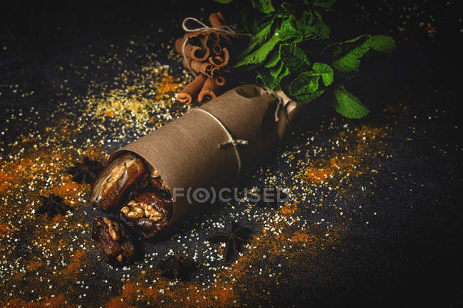 Dátiles secos, higos, menta fresca y canela para merienda halal para Ramadán envuelto en pergamino sobre fondo oscuro - foto de stock