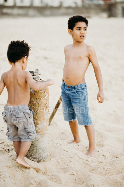 Deux frères afro-américains avec des bâtons jouant ensemble sur le rivage sablonneux près de la mer — Photo de stock