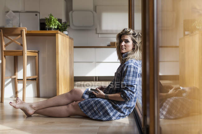 Mulher bonita e jovem sentada no chão de sua casa, olhando para a câmera — Fotografia de Stock