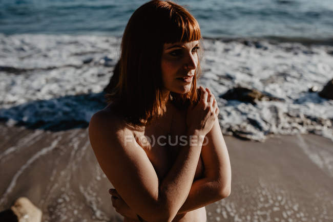 Привлекательная обнаженная женщина позирует возле морской воды на пляже в солнечный день — стоковое фото
