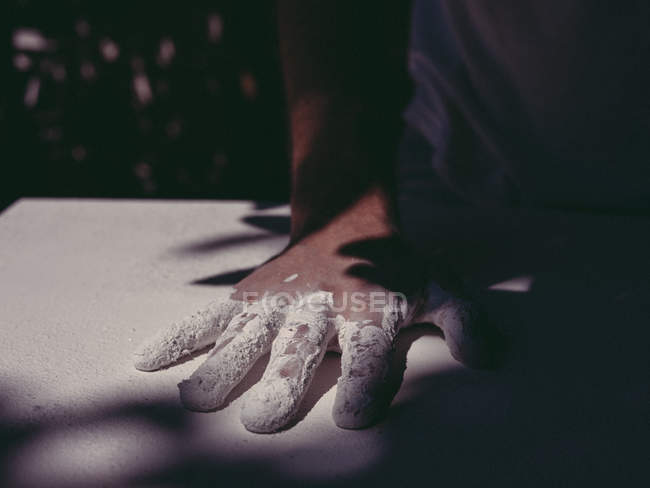 Рука анонимного художника-мужчины, распространяющего грубую белую штукатурку на ровную поверхность в мастерской — стоковое фото