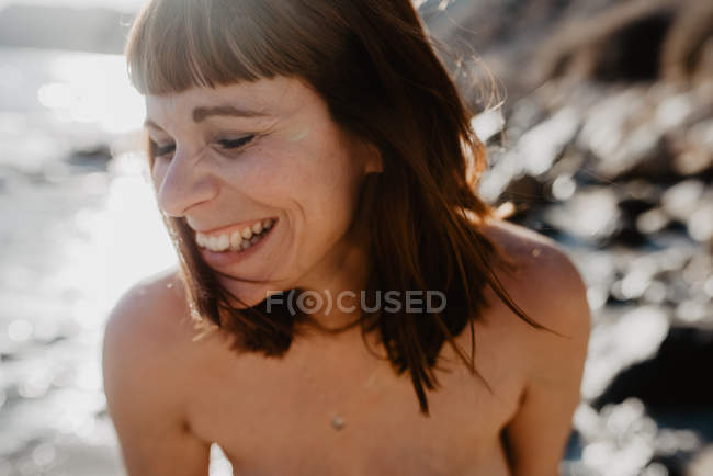 Adult woman keeping eyes closed and cheerfully smiling at seashore on sunny day in beach — Stock Photo