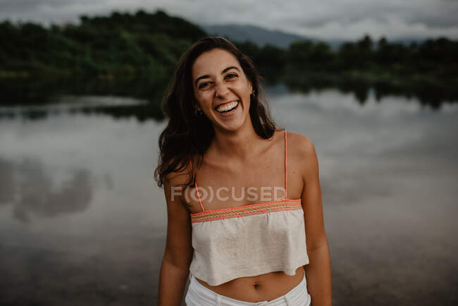Retrato de mujer sonriente cerca del estanque con aguas tranquilas en el campo - foto de stock