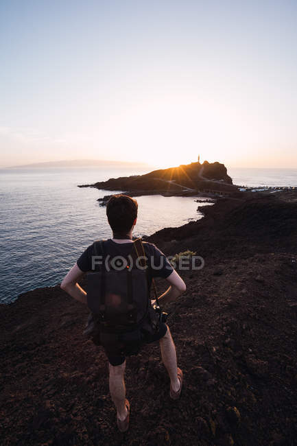 Homme randonneur regarder coucher de soleil au-dessus de la côte éloignée — Photo de stock