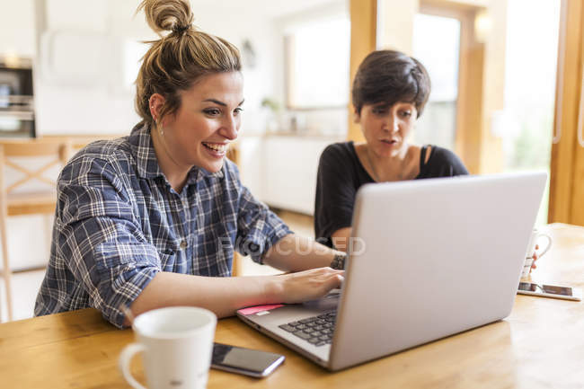 Due belle e giovani donne che fanno colazione a casa e utilizzano il computer portatile — Foto stock