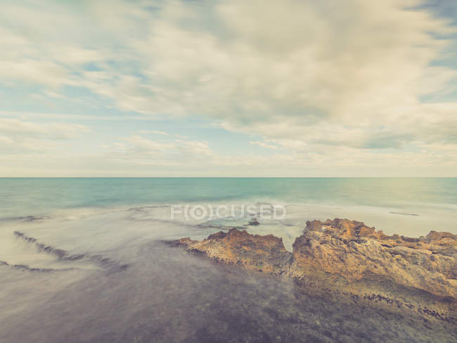 Costa rocciosa e blu mare schiumoso sullo sfondo del cielo con le nuvole — Foto stock