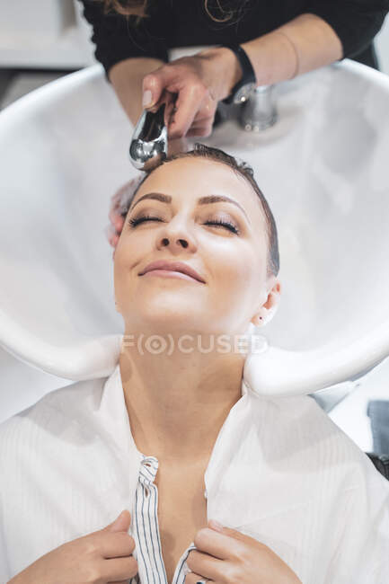 Stylist washing hairs to young lady — Stock Photo
