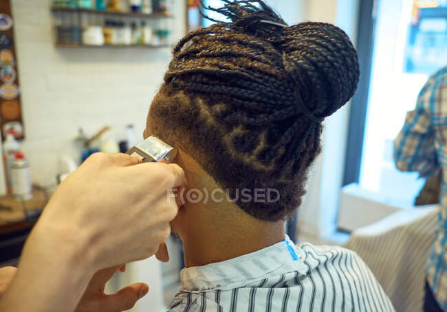 Вид на урожай со спины анонимного парикмахера, делающего современную стрижку бритвой безликому африканско-американскому клиенту — стоковое фото