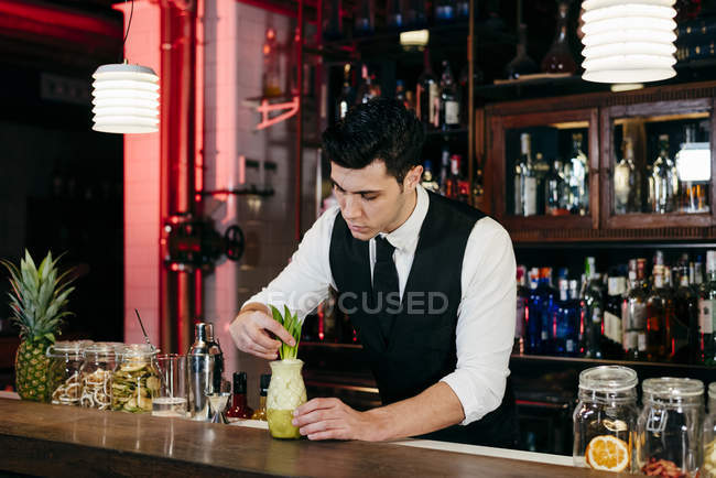 Jeune barman élégant travaillant derrière un comptoir de bar préparer une boisson dans un verre — Photo de stock