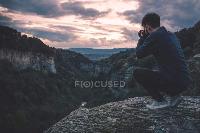 Мужчина с фотокамерой сидит на горе с великолепным закатом — стоковое фото