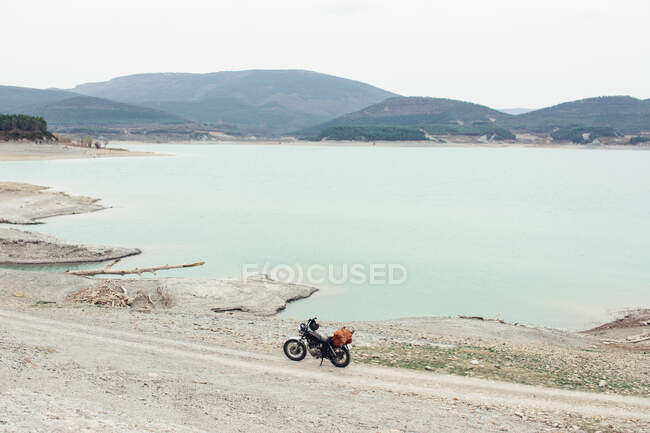 Motorbike parked on countryside road on shore of tranquil lake during trip in nature — Stock Photo