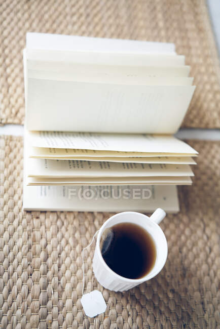 Муг свіжого теплого чаю розміщений на столі біля відкритої книги з цікавими історіями — стокове фото