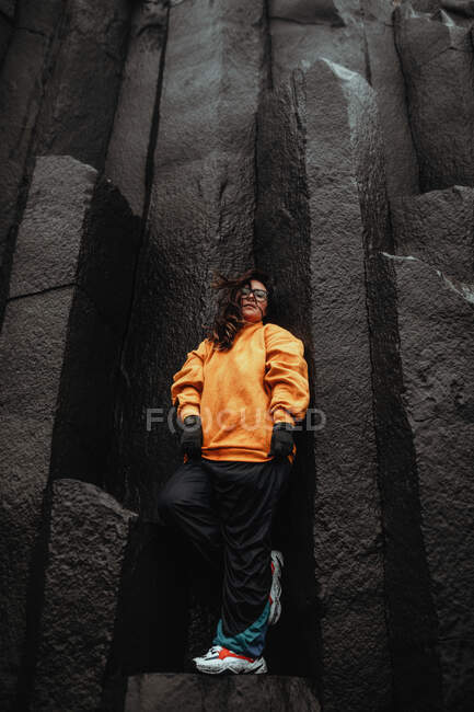 From below of young attractive female in trendy sportive clothes standing on black stone wall — Stock Photo