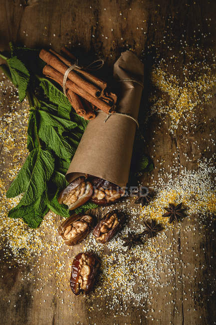 Dátiles secos, higos, menta fresca y canela para merienda halal para Ramadán envuelto en pergamino sobre mesa de madera - foto de stock