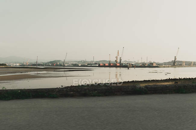 Industrial landscape with sea bay and port cranes in hilly terrain in cloudy day — Stock Photo