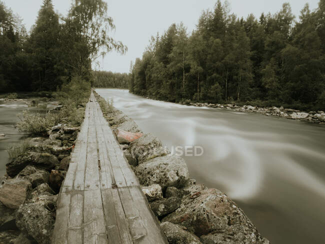Waldlandschaft mit hölzernem Fußweg zwischen Steinen am Fluss in Finnland bei bewölktem Tag — Stockfoto