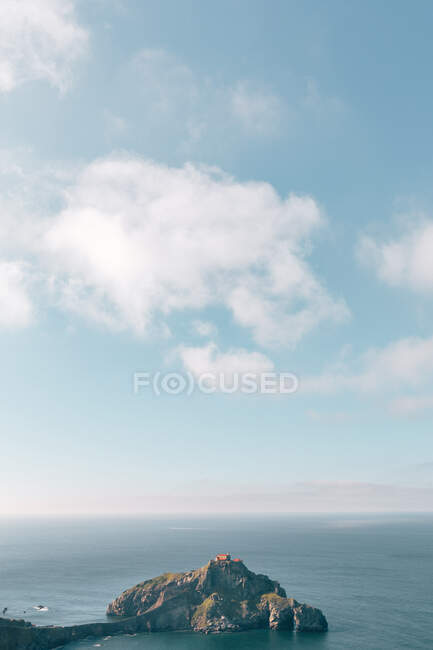 Pintoresca vista de roca con arcos naturales y casa en la parte superior rodeada de mar por la tarde en día nublado - foto de stock