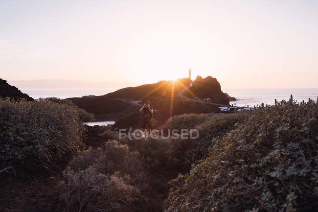 Мужчина-турист фотографирует во время прогулки по морю на закате — стоковое фото