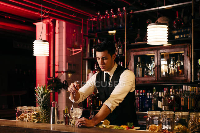 Молодой элегантный бармен, работающий за барной стойкой, смешивая напитки с фруктами — стоковое фото
