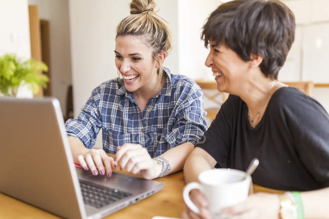 Two beautiful and young women having breakfast at home and using the laptop — Stock Photo