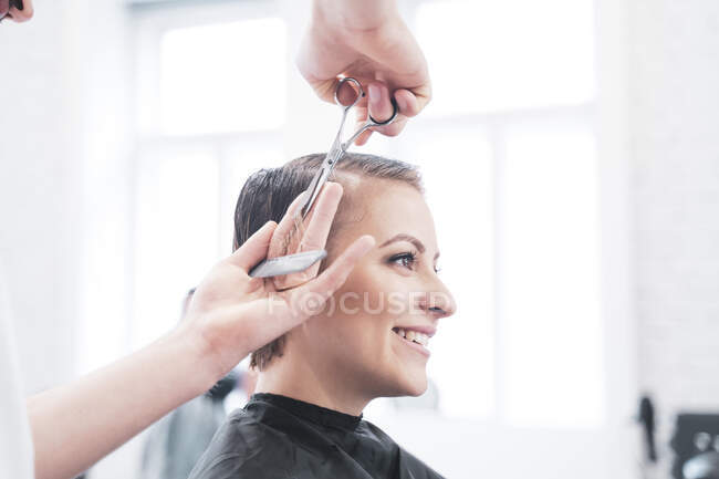 Peluquería corta el cabello de la mujer con tijeras - foto de stock