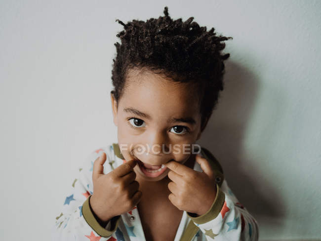 Adorable garçon afro-américain en pyjama regardant la caméra et faire un drôle de visage tout en se tenant contre le mur gris — Photo de stock
