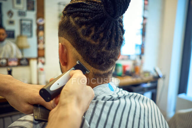 Crop view from behind of Anonymous hairstylist doing a modern haircut with a razor to a faceless african-american customer — Stock Photo