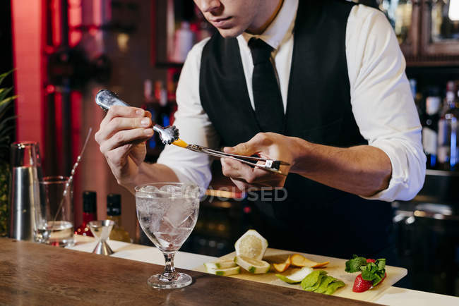Crop joven barman elegante anónimo trabajando detrás de un mostrador de bar mezclando bebidas con frutas - foto de stock