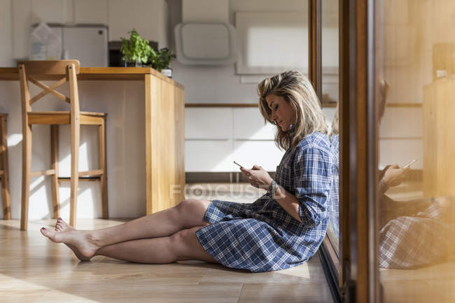 Bella e giovane donna seduta sul pavimento della sua casa sul cellulare — Foto stock