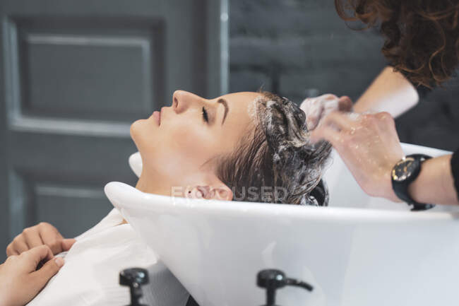 Stylist washing hairs to young lady — Stock Photo