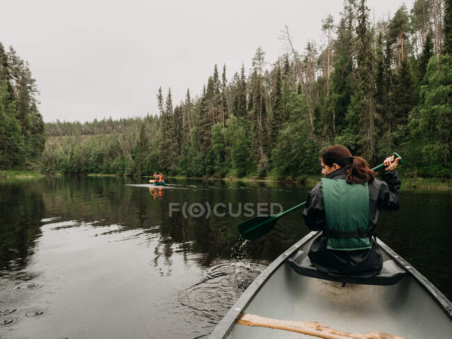 Back view of young woman while boating on forest river in Finland — Stock Photo