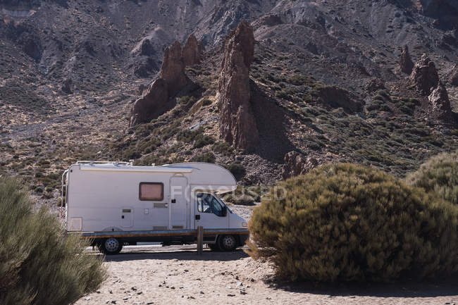 Caravana viajando na beira da estrada no deserto selvagem ao lado de arbustos no fundo da montanha pedregosa na luz do sol — Fotografia de Stock