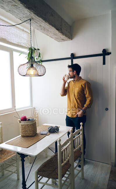 Adult male enjoying fresh hot tea and looking away while sitting at table near knitting needles and yarn — Stock Photo