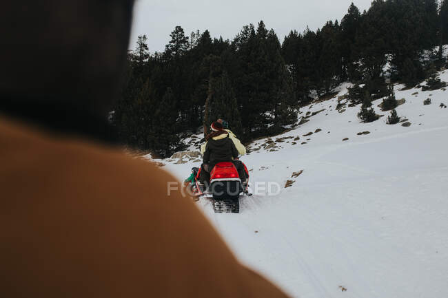Vista trasera de la gente en ropa de abrigo montando moto de nieve en la ladera de la montaña en maravilloso día de invierno - foto de stock