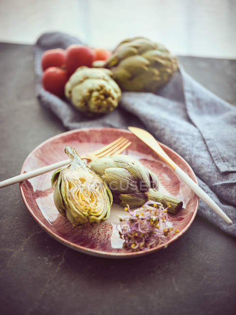 Whole and halved fresh artichokes placed on pink ceramic plate on table — Stock Photo