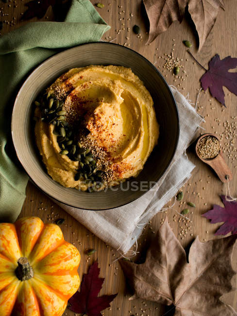 Набор вкусного тыквенного хумуса с семенами на салфетке на пилораме с сушеными осенними листьями — стоковое фото