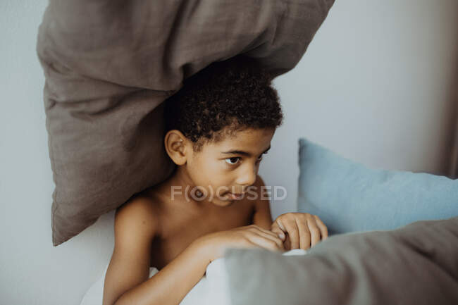 Criança deitada sob almofadas em cama confortável no quarto acolhedor — Fotografia de Stock