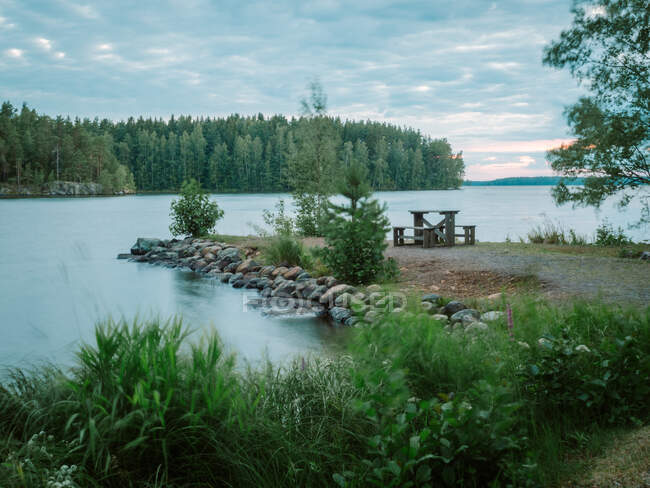 Peaceful landscape with forest, lake and wooden table and benches on lakeside headland in Finland — Stock Photo