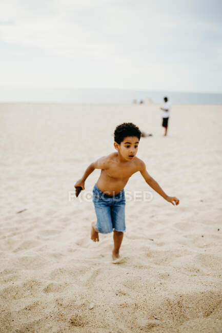 Lustiger afroamerikanischer Junge spielt am Sandstrand in der Nähe des Meeres — Stockfoto
