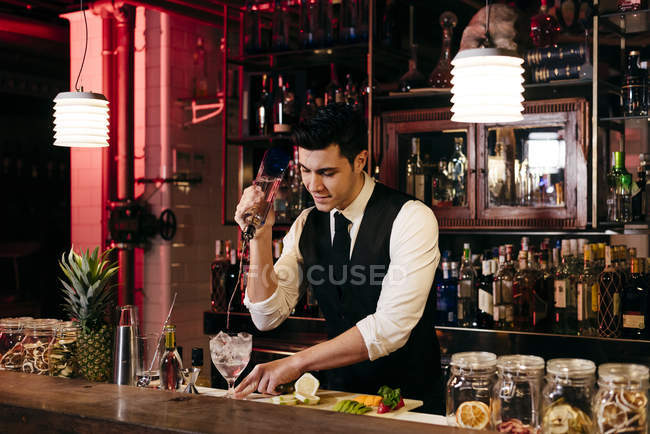 Joven barman elegante que trabaja detrás de un mostrador de bar mezclando bebidas con frutas - foto de stock