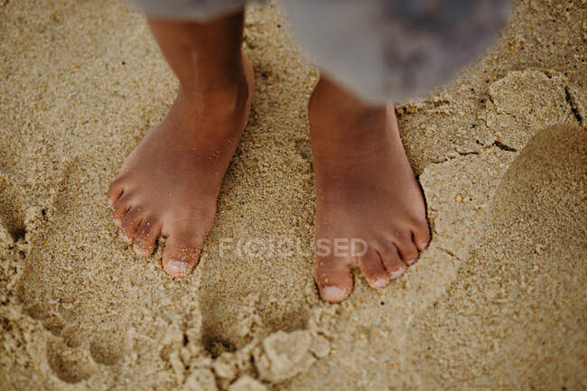 Ноги анонимного афроамериканского босоногого ребенка, стоящего на мокром песке на пляже — стоковое фото